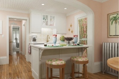 A pastel pink kitchen with a white island, floral barstools, and vintage-inspired decor featuring tropical accents and playful details.