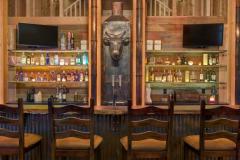 A view of the leather topped seating and washboard style accents on the front of a natural wood topped bar.