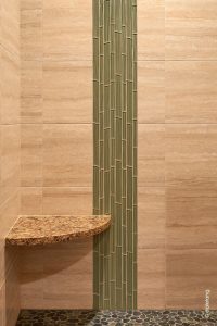 Green glass tile is inlayed vertically against neutral field tile to harken to bamboo poles in a curbless shower designed by Robin Rigby Fisher