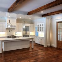 Bright kitchen design with custom ceiling and exposed beams, hardwood floors and white cabinets.