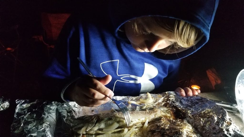 Boy eating fresh-caught fish for his camp dinner.