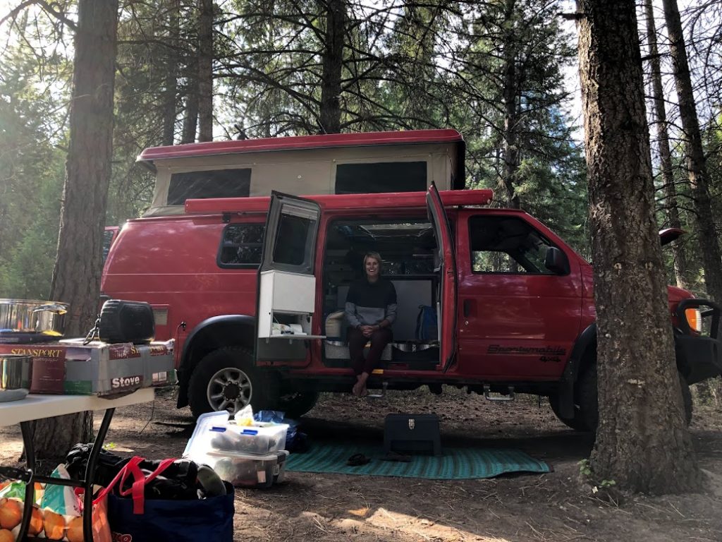 Woman sitting on the edge of her red camper van enjoying the van life.