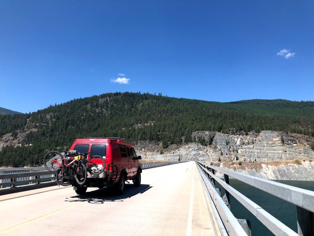 A 2001 Ford E350 extended body Sportsmobile with penthouse pop-top and a Quigley 4X4 conversion driving over a bridge.